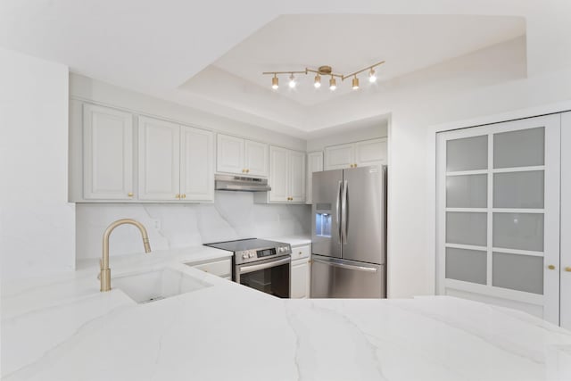 kitchen featuring white cabinetry, sink, a tray ceiling, stainless steel appliances, and light stone countertops