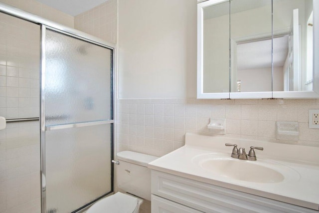 bathroom with vanity, toilet, a shower with shower door, and tile walls