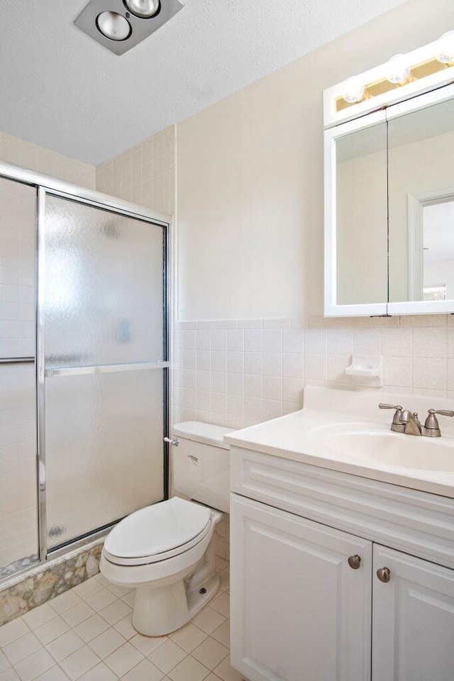 bathroom with tile patterned floors, vanity, a shower with door, tile walls, and toilet