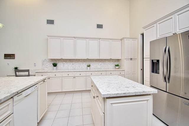 kitchen featuring white dishwasher, stainless steel fridge with ice dispenser, light tile patterned floors, decorative backsplash, and a high ceiling