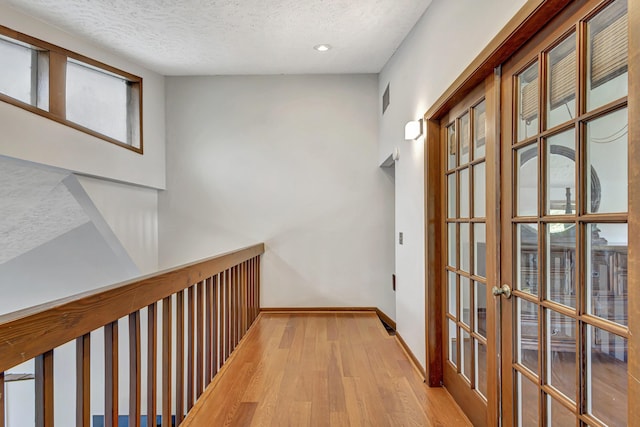 hallway featuring a textured ceiling, light hardwood / wood-style flooring, and french doors