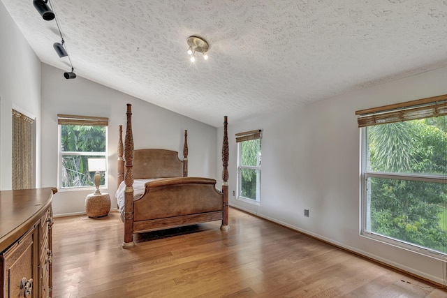 bedroom with a textured ceiling, light hardwood / wood-style flooring, and vaulted ceiling