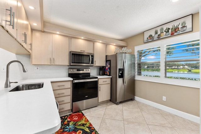 kitchen with light brown cabinets, sink, light tile patterned floors, a textured ceiling, and stainless steel appliances