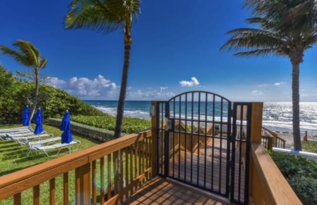 wooden terrace featuring a water view and a beach view