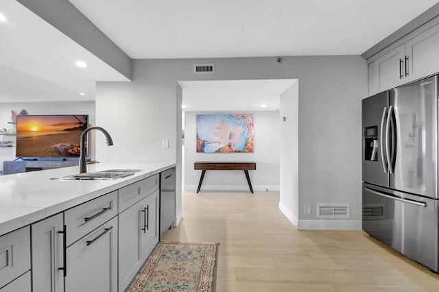 kitchen with appliances with stainless steel finishes, sink, gray cabinets, and light hardwood / wood-style floors