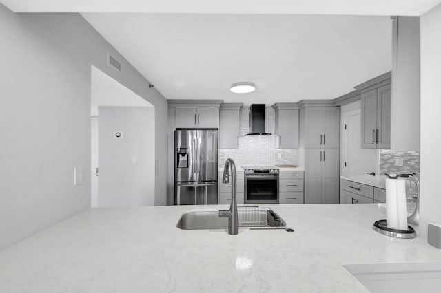 kitchen featuring appliances with stainless steel finishes, wall chimney exhaust hood, tasteful backsplash, sink, and gray cabinetry