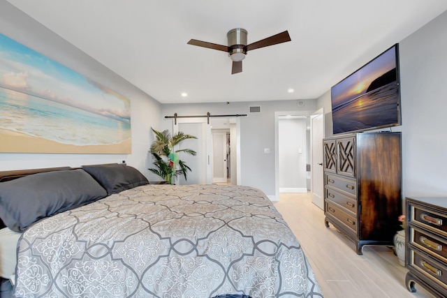 bedroom with ceiling fan, light hardwood / wood-style flooring, and a barn door