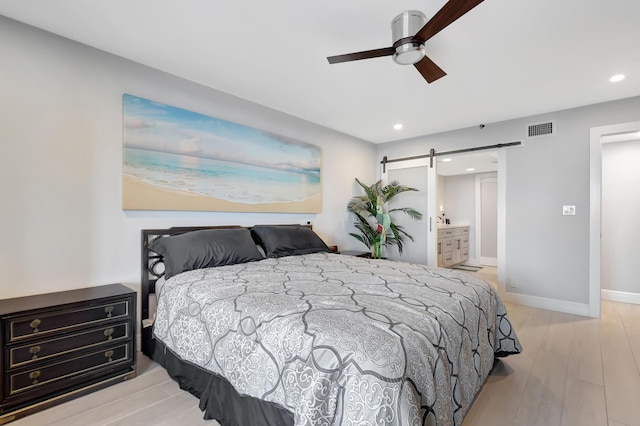 bedroom with ceiling fan, a barn door, connected bathroom, and light hardwood / wood-style flooring