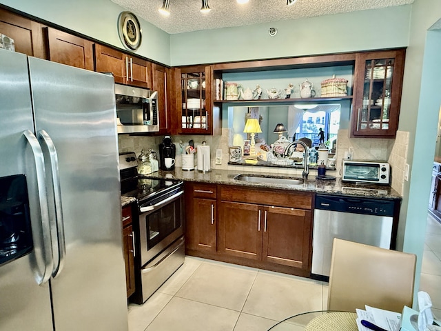 kitchen featuring sink, a textured ceiling, dark stone counters, stainless steel appliances, and backsplash