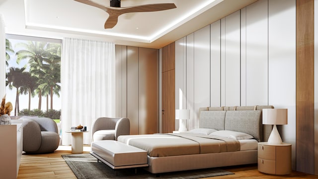 bedroom featuring ceiling fan, a tray ceiling, and light wood-type flooring