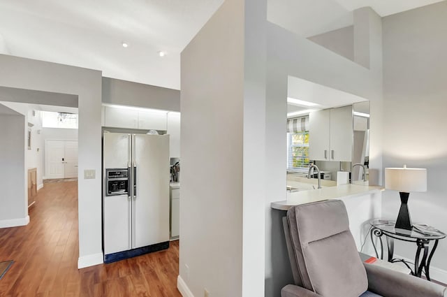 kitchen featuring hardwood / wood-style floors, kitchen peninsula, sink, white refrigerator with ice dispenser, and white cabinets