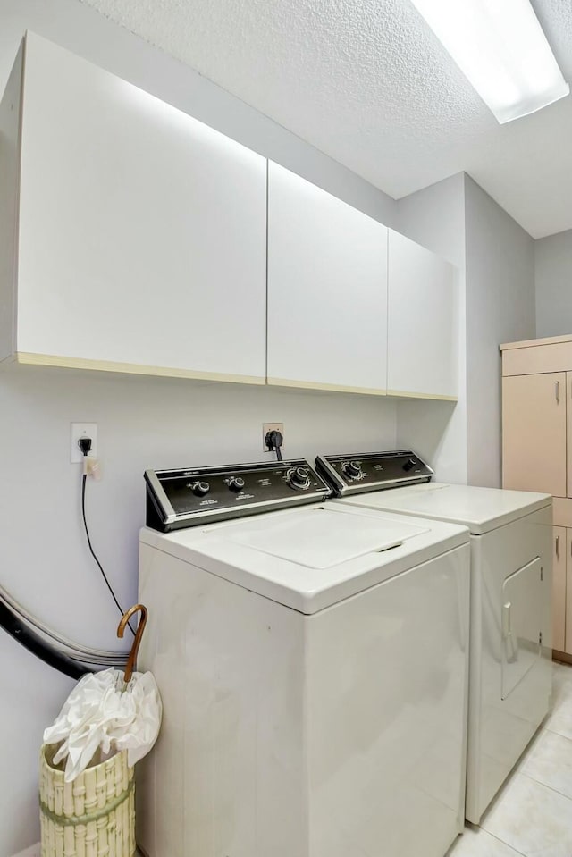 laundry room with washing machine and dryer, cabinets, light tile patterned floors, and a textured ceiling