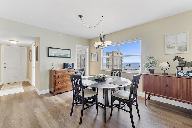 dining room with a water view, light hardwood / wood-style flooring, and a notable chandelier