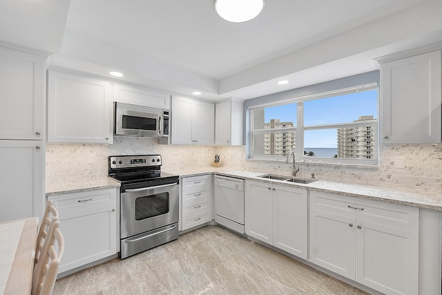 kitchen with white cabinets, appliances with stainless steel finishes, light stone countertops, and sink