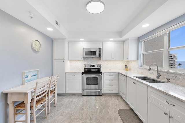 kitchen with white cabinetry, appliances with stainless steel finishes, sink, and light stone counters