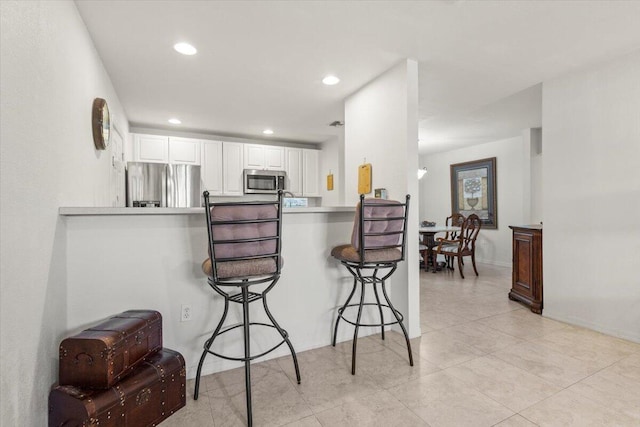 kitchen with a breakfast bar area, white cabinetry, kitchen peninsula, and appliances with stainless steel finishes