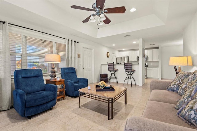 tiled living room with ceiling fan and a tray ceiling