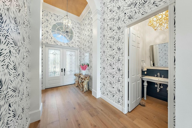 foyer entrance featuring a notable chandelier, crown molding, french doors, and light hardwood / wood-style flooring