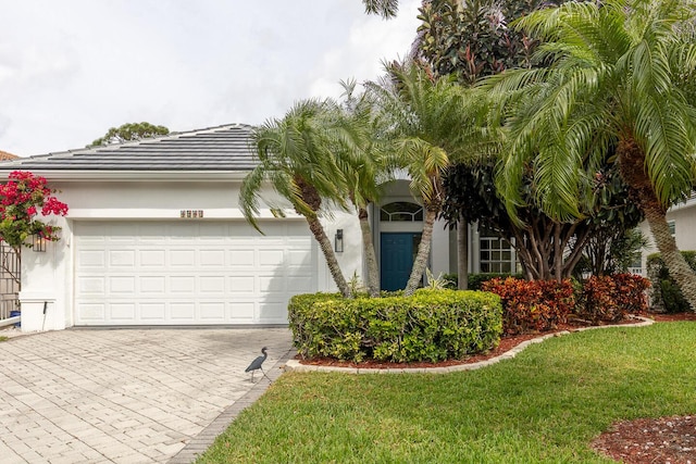 view of property hidden behind natural elements featuring a front lawn, decorative driveway, an attached garage, and stucco siding