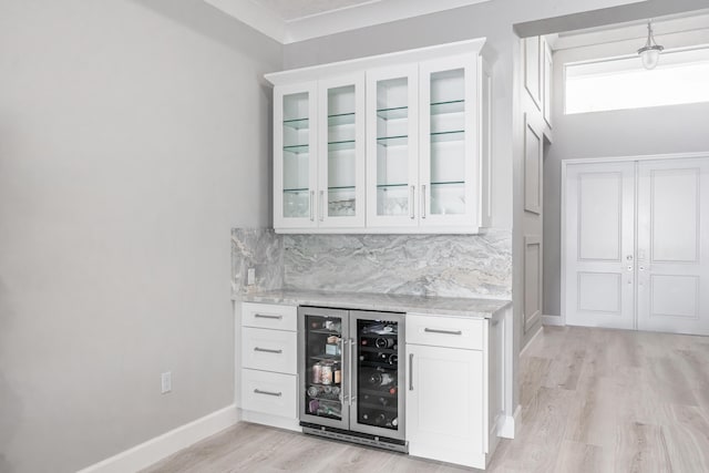 bar with wine cooler, backsplash, light hardwood / wood-style flooring, white cabinets, and light stone counters