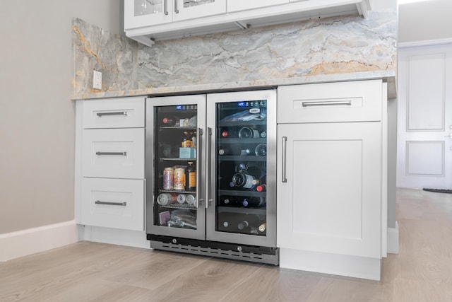 bar with decorative backsplash, beverage cooler, white cabinets, and light wood-type flooring