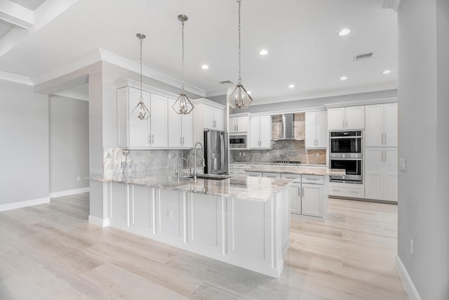 kitchen featuring decorative light fixtures, white cabinets, appliances with stainless steel finishes, and wall chimney exhaust hood