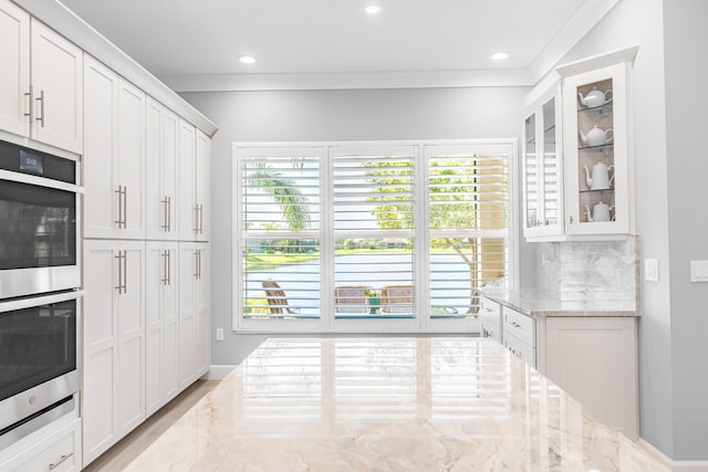 kitchen with light stone countertops, backsplash, white cabinets, and double oven