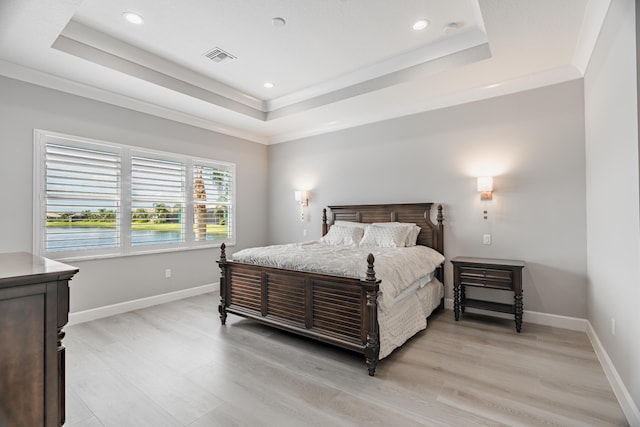 bedroom featuring ornamental molding, light hardwood / wood-style flooring, and a tray ceiling