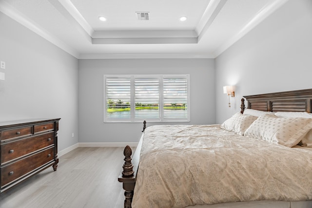 bedroom with ornamental molding, light hardwood / wood-style flooring, and a tray ceiling