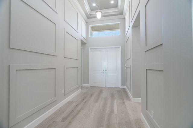 hall featuring a towering ceiling, light hardwood / wood-style flooring, and a tray ceiling