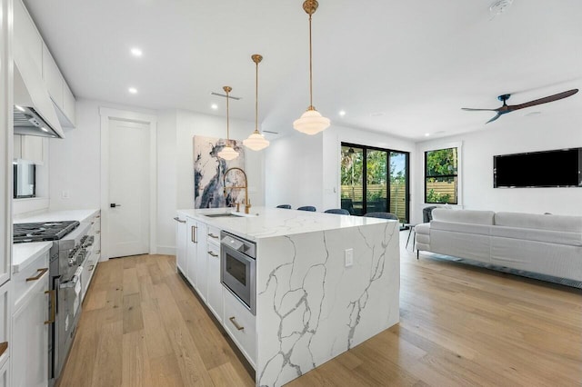 kitchen featuring a center island with sink, hanging light fixtures, light stone countertops, white cabinets, and sink