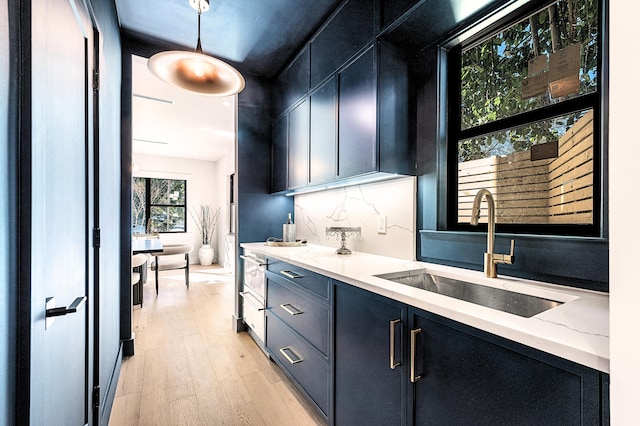 kitchen featuring light hardwood / wood-style floors, hanging light fixtures, light stone countertops, decorative backsplash, and sink