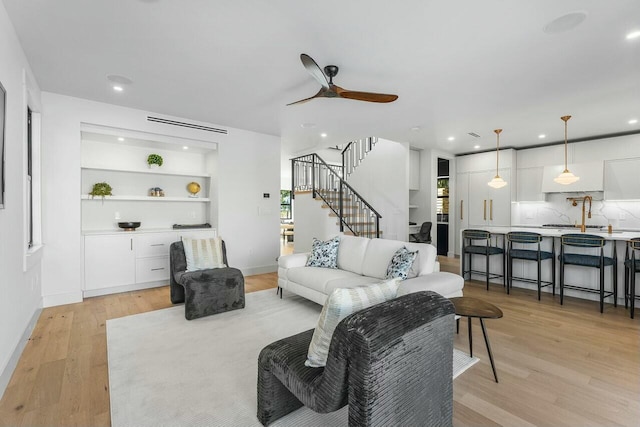 living room with light wood-type flooring, built in features, and ceiling fan