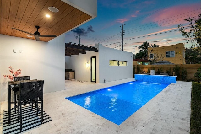 pool at dusk with ceiling fan, a patio area, pool water feature, and an outdoor structure