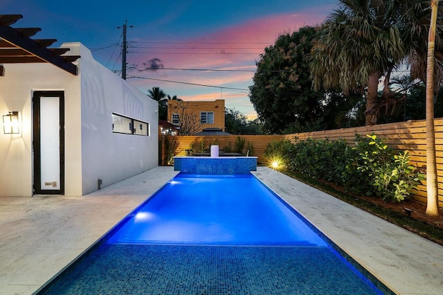 pool at dusk with pool water feature and a patio area