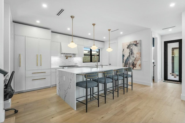 kitchen featuring a center island with sink, white cabinetry, pendant lighting, and light stone countertops