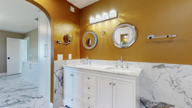 601 SE Karrigan Ter, Port Saint Lucie, FL 34983 - bathroom featuring marble look tiles, double vanity, a wainscoted wall, and tile walls
