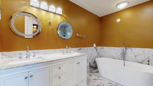 601 SE Karrigan Ter, Port Saint Lucie, FL 34983 - bathroom featuring marble finish floors, a freestanding tub, double vanity, a wainscoted wall, and tile walls