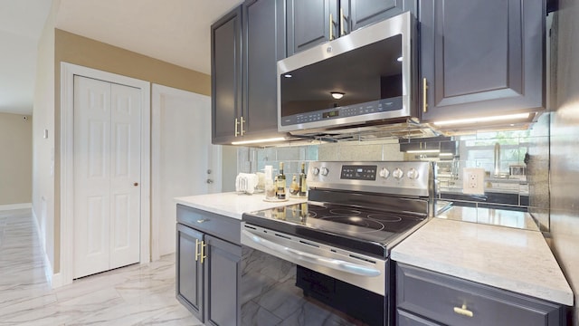 601 SE Karrigan Ter, Port Saint Lucie, FL 34983 - kitchen featuring appliances with stainless steel finishes, light marble finish flooring, light countertops, decorative backsplash, and gray cabinets