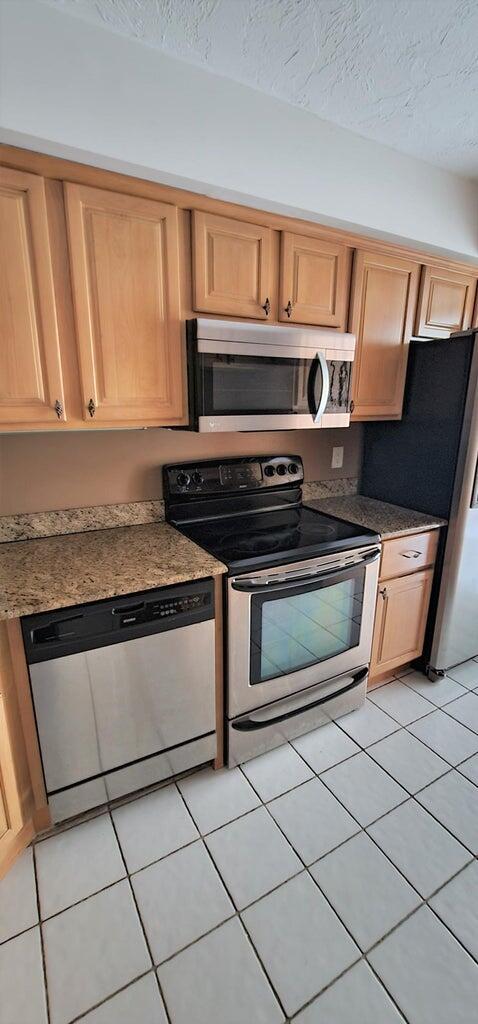 2425 Presidential Way Unit 402, West Palm Beach, FL 33401 - kitchen featuring appliances with stainless steel finishes, light tile patterned floors, light brown cabinets, and a textured ceiling
