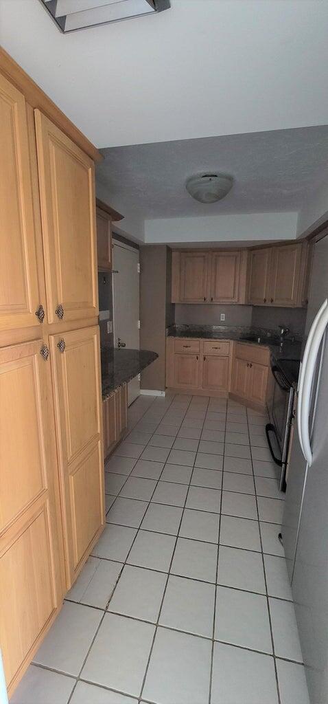 2425 Presidential Way Unit 402, West Palm Beach, FL 33401 - kitchen with light tile patterned floors, dark countertops, and freestanding refrigerator