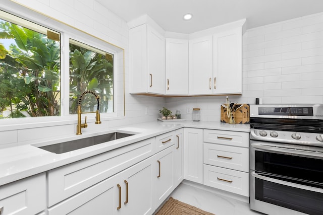 kitchen featuring sink, double oven range, white cabinetry, and backsplash