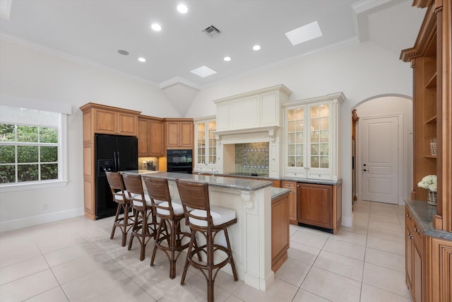 kitchen featuring light tile patterned flooring, a breakfast bar area, ornamental molding, a kitchen island, and black appliances