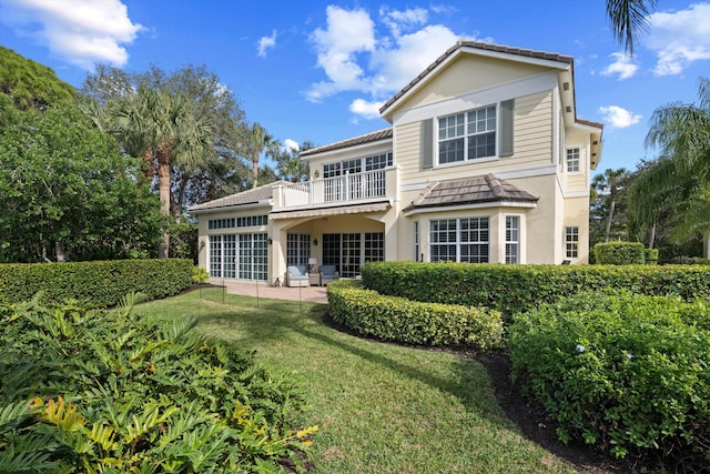 rear view of property featuring a lawn, a balcony, and a patio area