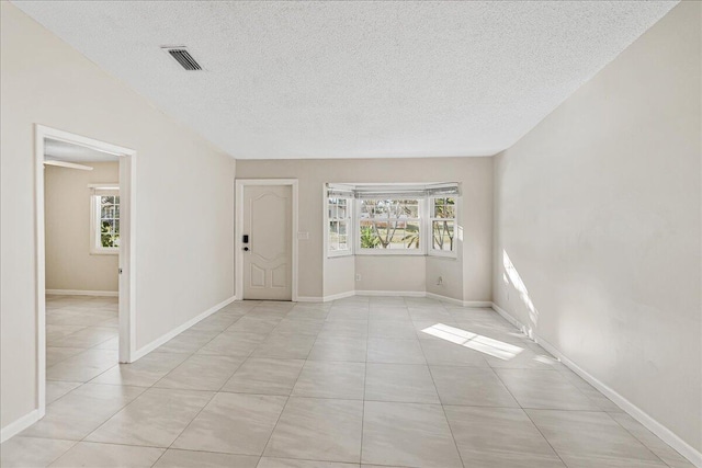 spare room with a textured ceiling, light tile patterned flooring, and a wealth of natural light