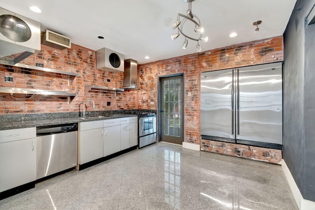 kitchen featuring wall chimney exhaust hood, hanging light fixtures, white cabinetry, appliances with stainless steel finishes, and sink