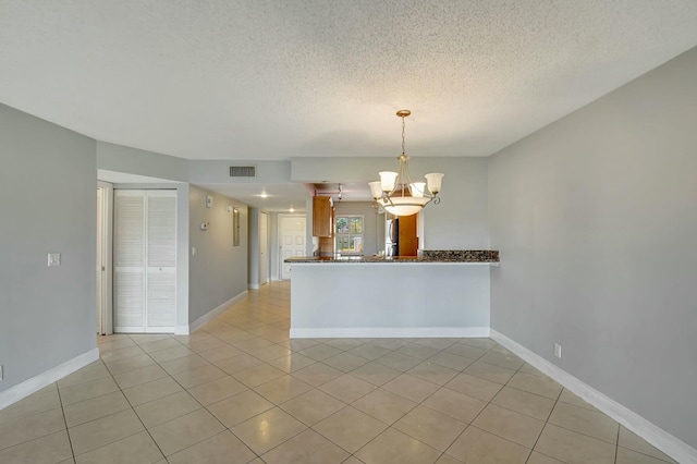 empty room with a textured ceiling, light tile patterned flooring, and a notable chandelier