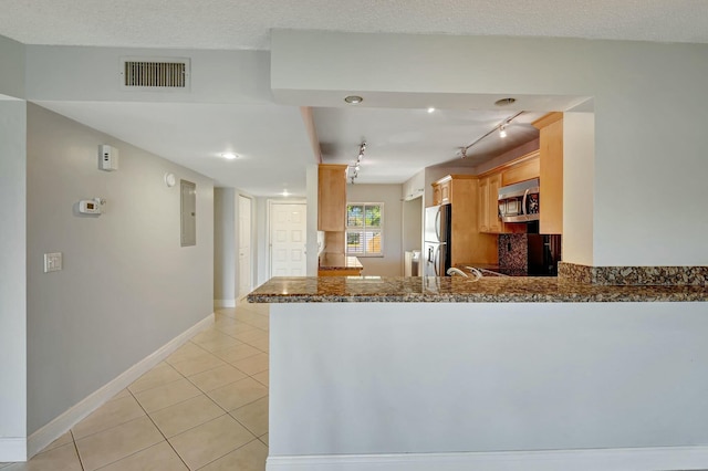 kitchen featuring kitchen peninsula, light tile patterned floors, backsplash, dark stone counters, and appliances with stainless steel finishes