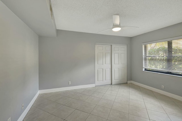 unfurnished bedroom with light tile patterned flooring, a textured ceiling, ceiling fan, and a closet