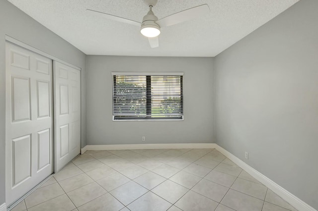 unfurnished bedroom with a textured ceiling, a closet, ceiling fan, and light tile patterned floors